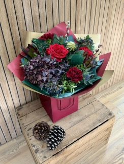 Luxury red Christmas bouquet with deep festive tones, winter textures and seasonal greenery arranged in a gift bag.