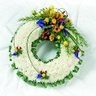White chrysanthemum funeral wreath with bold yellow, green, and red accents, creating a vibrant tribute.